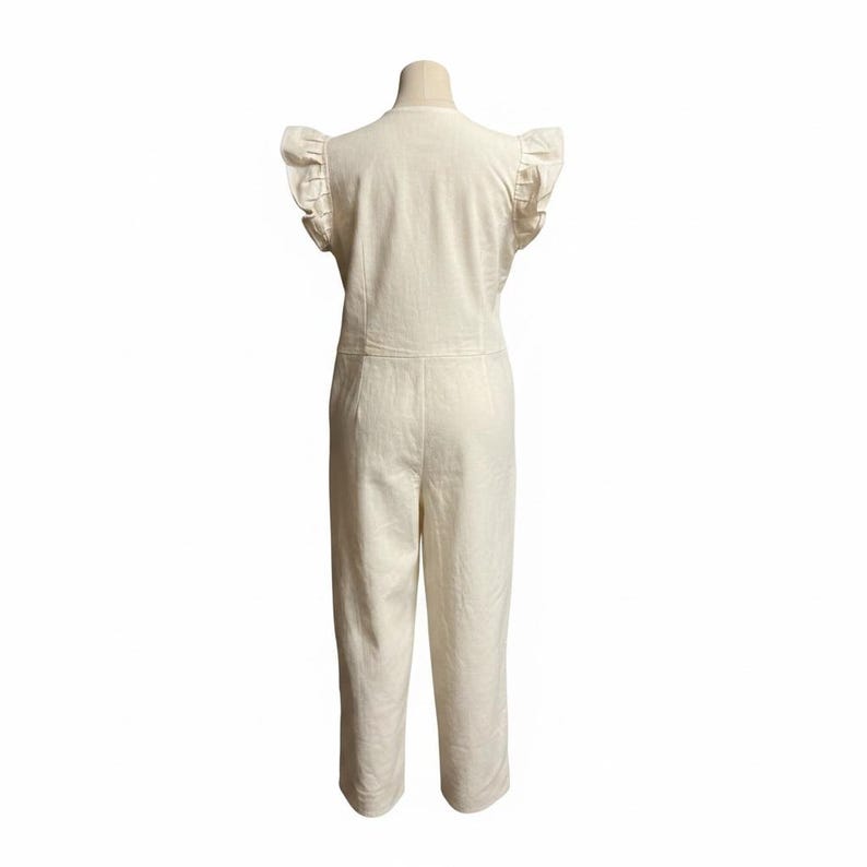 May include: An off-white jumpsuit featuring short flutter sleeves with ruffled edges, a round neckline, and a fitted bodice that transitions into straight-leg trousers. The garment is displayed on a mannequin, showcasing a clean, solid-coloured design.