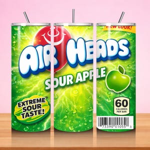 May include: A green Air Heads Sour Apple tumbler with a straw. The design features the Air Heads logo, a red smiling face, and a green apple graphic. Text includes "Extreme Sour Taste!" and "60 Calories Per Bar."