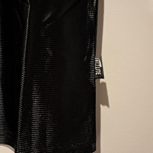 Op de afbeelding: Close-up van een zwart sportkledingstuk met een getextureerd, geribbeld patroon. Een klein label met het woord "CLIMALITE" in witte letters is aan het kledingstuk bevestigd.