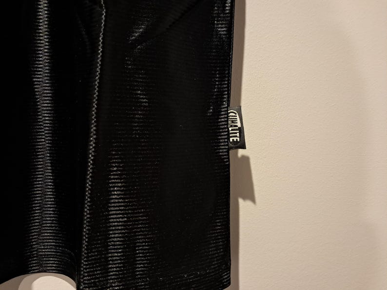 Op de afbeelding: Close-up van een zwart sportkledingstuk met een getextureerd, geribbeld patroon. Een klein label met het woord "CLIMALITE" in witte letters is aan het kledingstuk bevestigd.