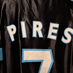 Op de afbeelding: Zwart shirt met de naam "PIRES" in witte letters met een lichtblauwe omlijning. Het nummer "7" is ook wit met een lichtblauwe omlijning. Het shirt heeft een mesh textuur.