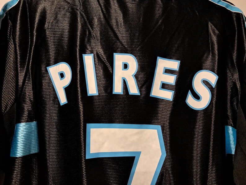 Op de afbeelding: Zwart shirt met de naam "PIRES" in witte letters met een lichtblauwe omlijning. Het nummer "7" is ook wit met een lichtblauwe omlijning. Het shirt heeft een mesh textuur.