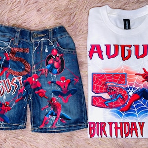 Peut inclure: Un short en jean bleu fonc&eacute; avec le texte rouge paillet&eacute; AUGUST et le chiffre 5, ainsi que plusieurs graphismes de Spider-Man. &Agrave; c&ocirc;t&eacute; se trouve un t-shirt blanc avec le texte AUGUST, 5 et BIRTHDAY BOY, illustr&eacute; avec Spider-Man.