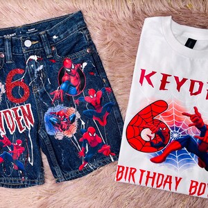 Peut inclure: Un short en jean bleu fonc&eacute; et un t-shirt blanc avec des motifs Spider-Man. Le short pr&eacute;sente un chiffre 6 rouge paillet&eacute;, le nom KEYDEN et des &eacute;claboussures de peinture blanche. Le t-shirt affiche le nom KEYDEN, un chiffre 6 rouge et BIRTHDAY BOY.