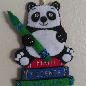 May include: A black and white panda holding a green crayon, sitting on top of a stack of books that say "MATH", "SCIENCE", and "ENGLISH".