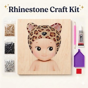 May include: A Rhinestone Craft Kit featuring a wooden board with a printed baby figure wearing a leopard-print hat. Includes three bags of rhinestones in gold, black, and silver, a pink applicator tool, a tube of B-7000 glue, and a purple tray.