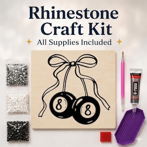 May include: Rhinestone craft kit with all supplies included. The kit features a wooden board with a black and white drawing of two eight balls tied with a bow. Includes bags of rhinestones, glue, a stylus, and a purple tray.