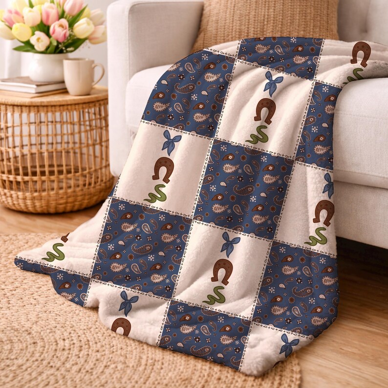May include: A soft fleece throw blanket featuring a patchwork design of alternating squares. One set of squares has a dark blue background with a brown and white paisley pattern. The other squares are cream with brown horseshoes, green snakes, and blue bows.