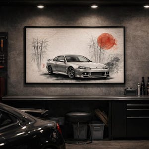 May include: A framed artwork depicting a silver sports car with a red sun and bamboo in the background. The artwork hangs in a garage setting with tools, tires, and a black car in the foreground. The garage has a concrete wall.
