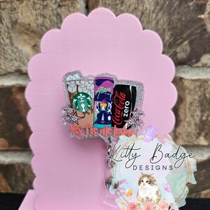 May include: An acrylic badge reel featuring a glittery design of three beverage containers: a Starbucks iced coffee, an Alani energy drink, and a Coca-Cola Zero can. The text "Yes, I've ate today" is printed in orange at the bottom of the graphic.
