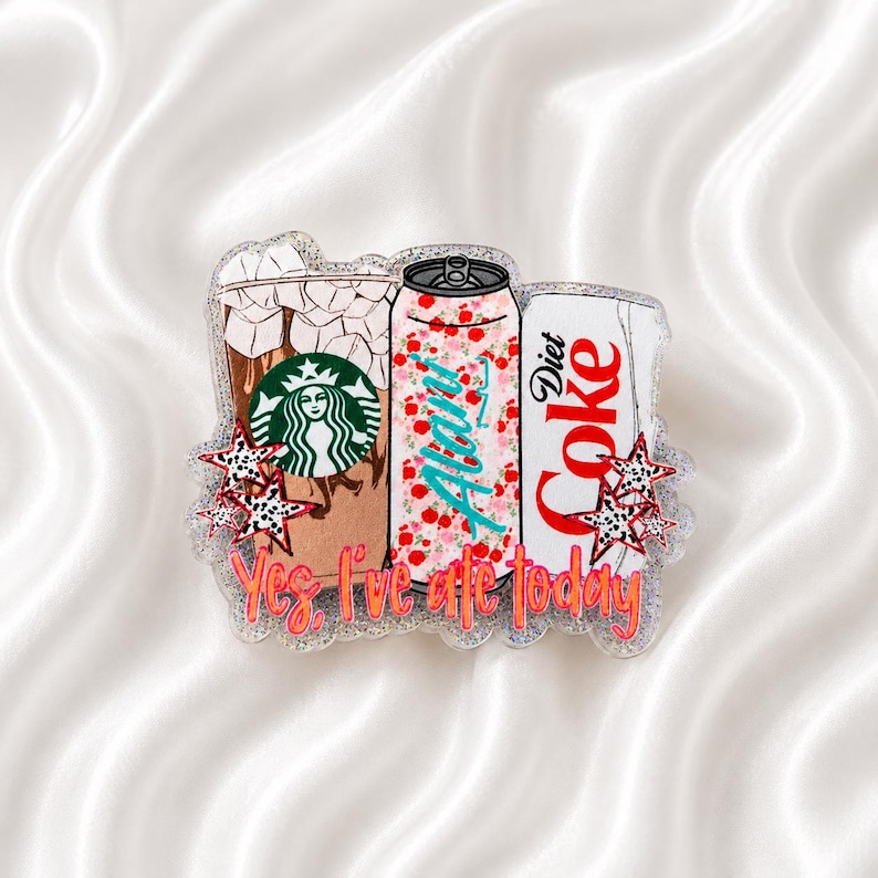 May include: A glittery acrylic badge featuring a Starbucks iced coffee, an Alani Nu energy drink, and a Diet Coke can. The design includes small leopard print stars and the orange text Yes, I've ate today printed across the bottom of the items.