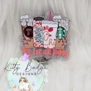 May include: A glittery acrylic badge reel featuring illustrations of three beverage cups and a soda can with the text Yes, I've ate today. The design includes a 7-Eleven logo, a floral Alani can, a Chick-fil-A cup, and a Starbucks logo.