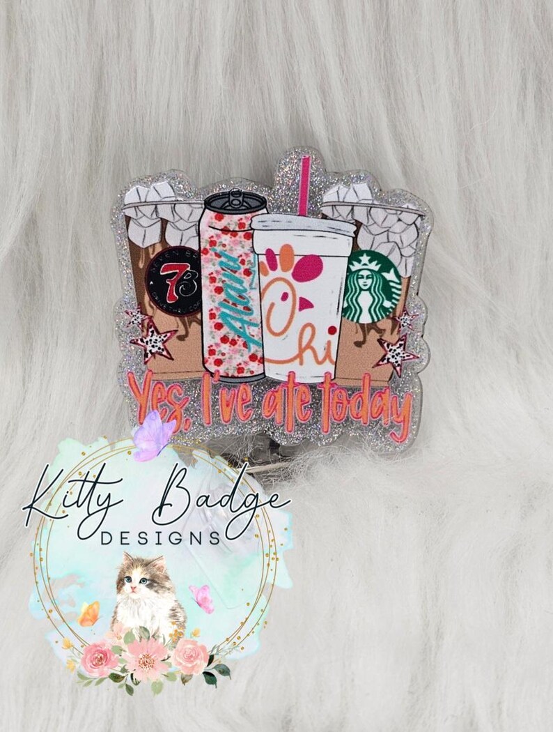 May include: A glittery acrylic badge reel featuring illustrations of three beverage cups and a soda can with the text Yes, I've ate today. The design includes a 7-Eleven logo, a floral Alani can, a Chick-fil-A cup, and a Starbucks logo.