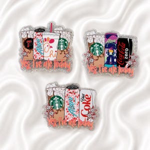 May include: Three glittery acrylic pins featuring illustrations of iced coffee cups, soda cans, and energy drinks. Each pin displays the text Yes, I've ate today in orange script, accented with small star shapes and various beverage brand logos.