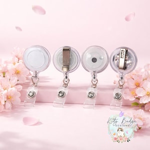 May include: Four circular badge reels with clear plastic housings and metal belt clips on the back. Each reel features a retractable cord attached to a clear vinyl strap with a metal snap button. The logo Kitty Badge Designs is visible.