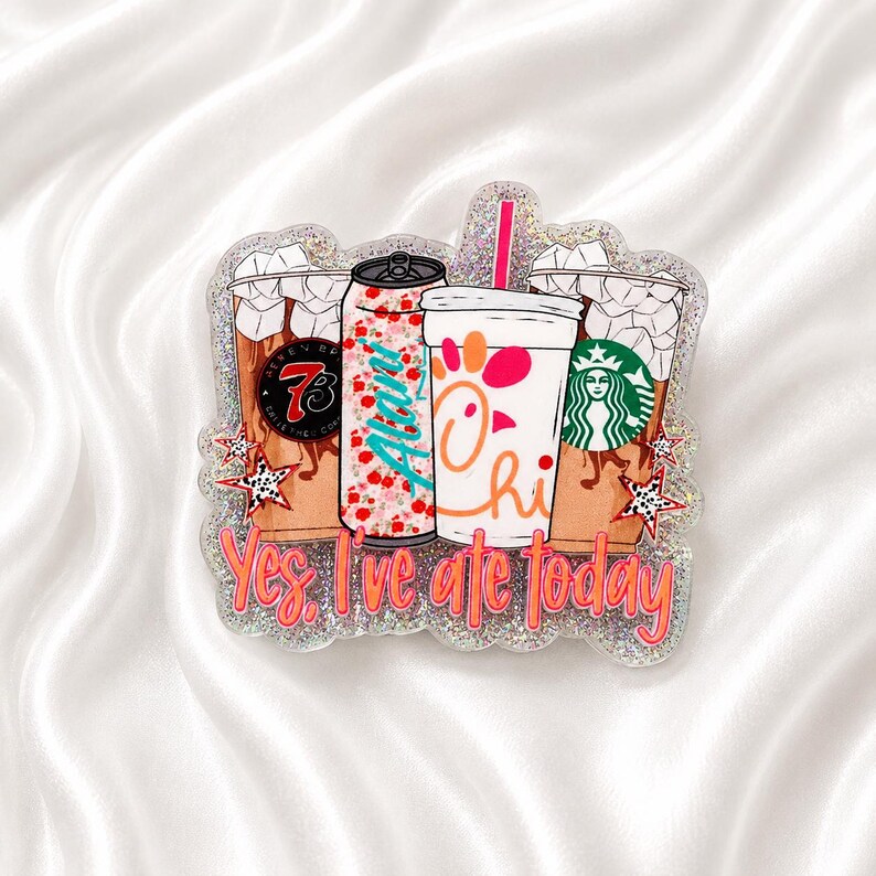 May include: A glittery acrylic badge featuring illustrations of four beverage containers, including a soda can and cups with logos. The text "Yes, I've ate today" is printed in orange at the bottom. The design includes star accents and a pink straw.