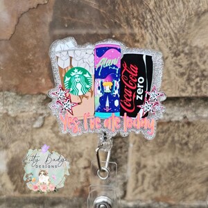 May include: A glittery acrylic badge reel featuring three beverage containers: a Starbucks iced coffee, an Alani energy drink, and a Coca-Cola Zero can. The design includes small pink star accents and the text Yes, I've ate today in orange.