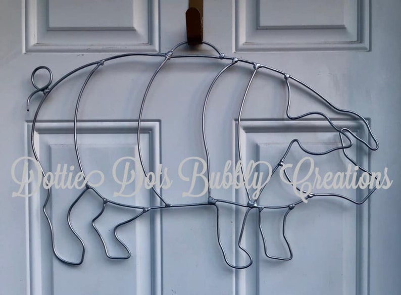 May include: A silver metal pig sculpture, shaped like a pig, with a curled tail. The pig is hanging on a white door.