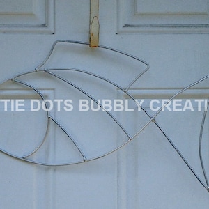 May include: A silver wire fish sculpture hanging on a white door. The sculpture is made of thin wire and has a simple, elegant design. The text "DOTTIE DOTS BUBBLY CREATIONS" is visible on the door.