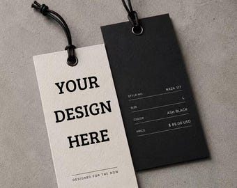 May include: Two rectangular paper hang tags with black string loops. The left tag is off-white with the black text YOUR DESIGN HERE and DESIGNED FOR THE NOW. The right tag is black with white text fields for STYLE NO. NX24-117, SIZE L, COLOR ASH BLACK, and PRICE $ 89.00 USD.
