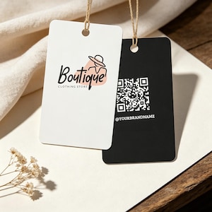 May include: Two rectangular clothing tags with rounded corners, one white and one black, suspended by twine. The white tag features a logo with the text Boutique CLOTHING STORE and a line-art illustration. The black tag displays a QR code and the text @YOURBRANDNAME.