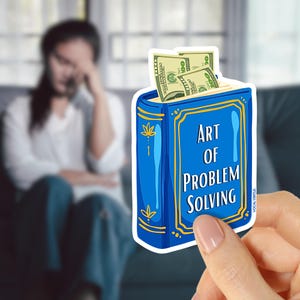 May include: A blue sticker in the shape of a book with the text "Art of Problem Solving" and a gold border. The book has money sticking out of the top. The sticker is held by a hand.