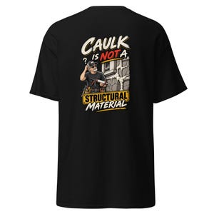 Könnte beinhalten: Ein schwarzes T-Shirt mit einer Grafik auf der Rückseite, die einen Bauarbeiter mit einer Kartuschenpistole zeigt, sowie weißem und gelbem Text: CAULK IS NOT A STRUCTURAL MATERIAL. Der Arbeiter trägt eine Kappe und einen Werkzeuggürtel an einer Wand.