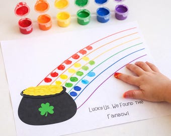 Può includere: Un progetto artistico a tema San Patrizio con un arcobaleno fatto di impronte digitali e un vaso d'oro. Le parole "Lucky Us... We Found the Rainbow!" sono stampate sulla carta. Barattoli di vernice di vari colori sono disposti sopra.
