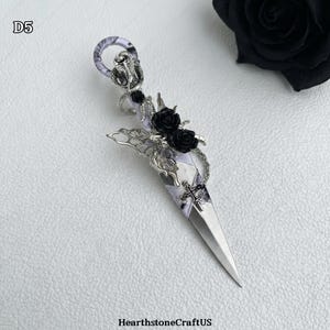 May include: A decorative dagger with a silver blade and ornate handle. The handle features a snake, black roses, and a cross design. The dagger is embellished with silver filigree and a patterned fabric wrap. The text "D5" is in the upper left corner.