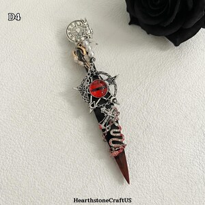 May include: A decorative dagger with a black handle and a red, pointed blade. The dagger features ornate silver-colored embellishments, including a red eye, a clock, and a snake design. The text "HearthstoneCraftUS" is at the bottom.