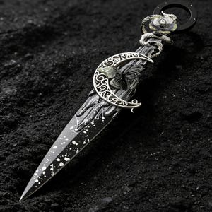 Peut inclure: Un poignard décoratif avec une lame et un manche noirs, orné d'un croissant de lune et d'un papillon argentés. La poignée est ornée d'un serpent et d'une rose argentés. Le poignard présente des éclaboussures de peinture blanche et un anneau en haut.