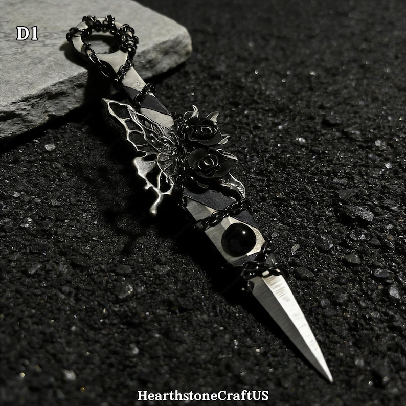 May include: A silver dagger with a black handle, adorned with a butterfly, roses, and a black gem. The dagger is embellished with a chain and has a sharp, pointed blade. The text "D1" is in the upper left corner.
