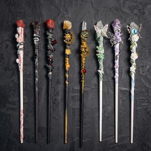 Pode incluir: Uma coleção de oito varinhas decorativas com vários designs. Cada varinha apresenta uma gema diferente no topo e é adornada com detalhes intrincados como cobras, borboletas e detalhes florais. As varinhas são em várias cores, incluindo branco, preto, dourado e roxo.