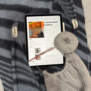 May include: A close-up of a knitting project featuring a striped blue and gray mohair garment. A tablet displays a pattern for a "Cool Girl Mohair Bandana." A ball of gray yarn and knitting needles are also visible.