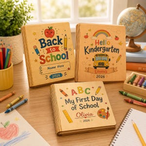 Könnte beinhalten: Drei quadratische Holzschilder mit Illustrationen und Text zum Thema Schule. Die Schilder tragen die Aufschriften Back to School, Hello Kindergarten und My First Day of School, verziert mit Äpfeln, Stiften, einem Schulbus und dem Jahr 2026.