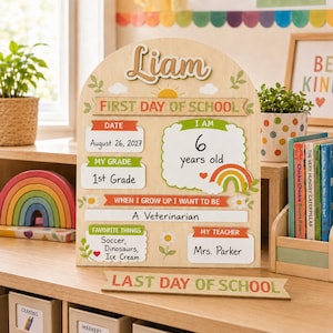 Könnte beinhalten: Ein bogenförmiges Holzschild für den ersten Schultag mit dem Namen Liam, einer Sonne und einem Regenbogen. Es enthält Felder für Datum, Klasse, Alter, Berufswunsch, Lieblingsdinge und Lehrer sowie ein separates Holzschild mit der Aufschrift Last Day of School.