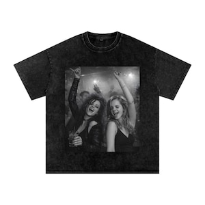 May include: Black and white graphic tee featuring a photo of two people dancing and smiling at a party. The t-shirt has a vintage, washed-out look.