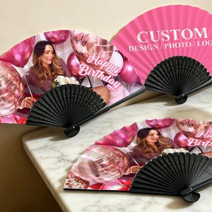 May include: Three black-handled folding fans. Two fans feature a photo of a woman with pink balloons and the text "Happy Birthday". The third fan is pink with the text "CUSTOM DESIGN/PHOTO/LOGO".