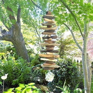 May include: A vertical hanging mobile composed of numerous smooth, weathered driftwood pieces of varying brown and gray tones, strung together in a column, terminating with a single, textured, light-colored stone at the bottom end.