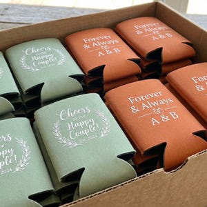Bulk custom wedding can coolers packed and ready to ship, featuring sage green and terracotta neoprene sleeves with cheers to the happy couple and forever and always messages. Perfect for fall weddings, outdoor receptions, and rustic venues. Made to order with crisp professional printing for consistent results. These reusable drink sleeves simplify event planning while offering guests a practical favor they can enjoy long after the wedding day has passed.