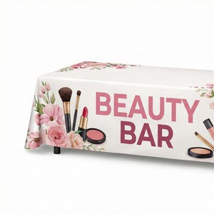 May include: A white rectangular tablecloth with the words "BEAUTY BAR" in pink. The tablecloth is decorated with pink roses and makeup items such as brushes, lipsticks, and compacts. The table has black legs.