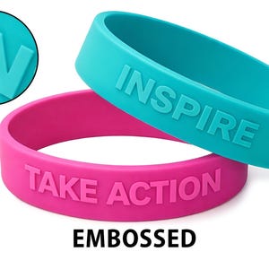 May include: Two embossed silicone wristbands, one teal and one pink, with the words "INSPIRE" and "TAKE ACTION" embossed on them. A close-up shows the word "IN" in teal. The word "EMBOSSED" is below the bracelets.
