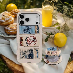 Puede incluir: Una funda de teléfono de color claro con tres ilustraciones estilo caja de cerillas con la marca New York Yankees, que incluyen un jugador de béisbol, un logotipo de equipo y un horizonte urbano. Un soporte circular a juego está situado cerca.