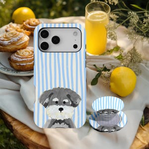 Könnte beinhalten: Ein Handyhülle mit blau-weißem Streifendesign und einer Schnauzer-Hundeillustration. Ein passender Handyhalter ist ebenfalls zu sehen. Das Bild zeigt Gebäck, ein Glas Orangensaft und Zitronen, was auf ein Picknick hindeutet.