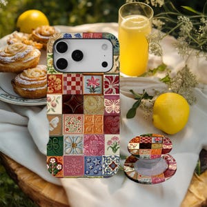 Puede incluir: Una funda de teléfono colorida y un agarre a juego con un diseño de patchwork de azulejos florales, geométricos y en forma de corazón. La funda está sobre una superficie blanca con un vaso de zumo de naranja, un limón y pasteles.