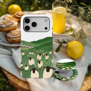 Puede incluir: Funda de teléfono blanca con una escena pastoral de ovejas pastando en una ladera verde. También se ve un soporte para teléfono a juego. La escena incluye colinas verdes, árboles en flor rosas y un rebaño de ovejas.