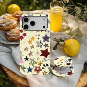 May include: A cream phone case and pop socket featuring a pattern of colourful stars. The stars are in various colours and textures, including red, blue, and gold. The case is shown with a glass of orange juice and a lemon.
