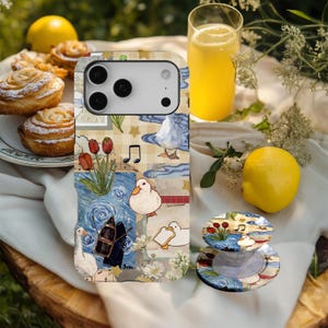May include: A phone case and pop socket with a whimsical design featuring ducks, musical notes, and floral elements. The case has a collage-like pattern with blue, white, and yellow accents. A glass of orange juice and pastries are also visible.