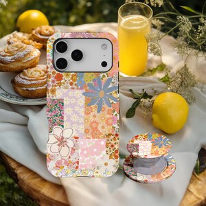 May include: A floral patchwork phone case and matching phone grip. The case features a variety of colourful flowers in pink, orange, and blue. The phone grip is a round, collapsible stand with a similar floral design.