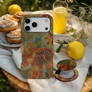 May include: A phone case and phone grip with a colorful, artistic design featuring suns, figures, and floral elements. The case is on a white surface with a glass of orange juice, lemons, and pastries.